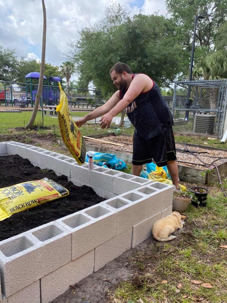 一名男子将一袋肥料堆肥扔进煤渣砖堆砌的花园床上